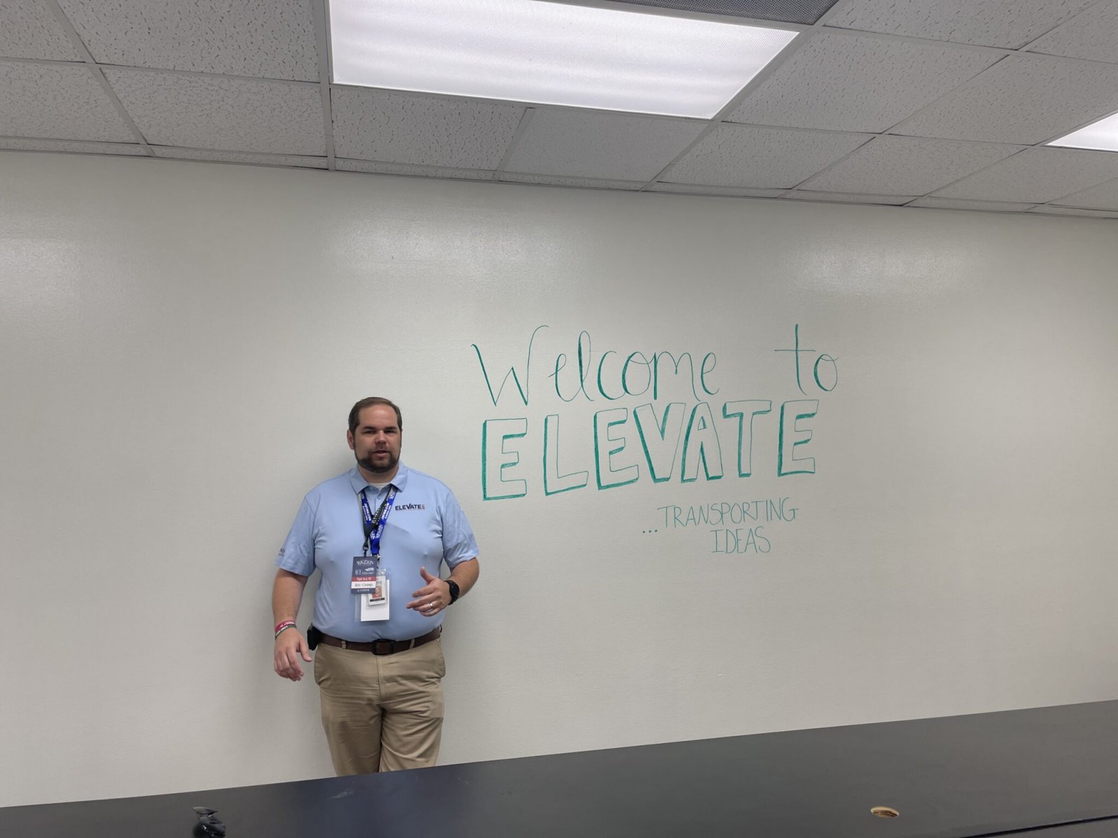 Eric Crump stands in front of white board at ELEVATE Incubator. White board says "Welcome to Elevate...transporting ideas."